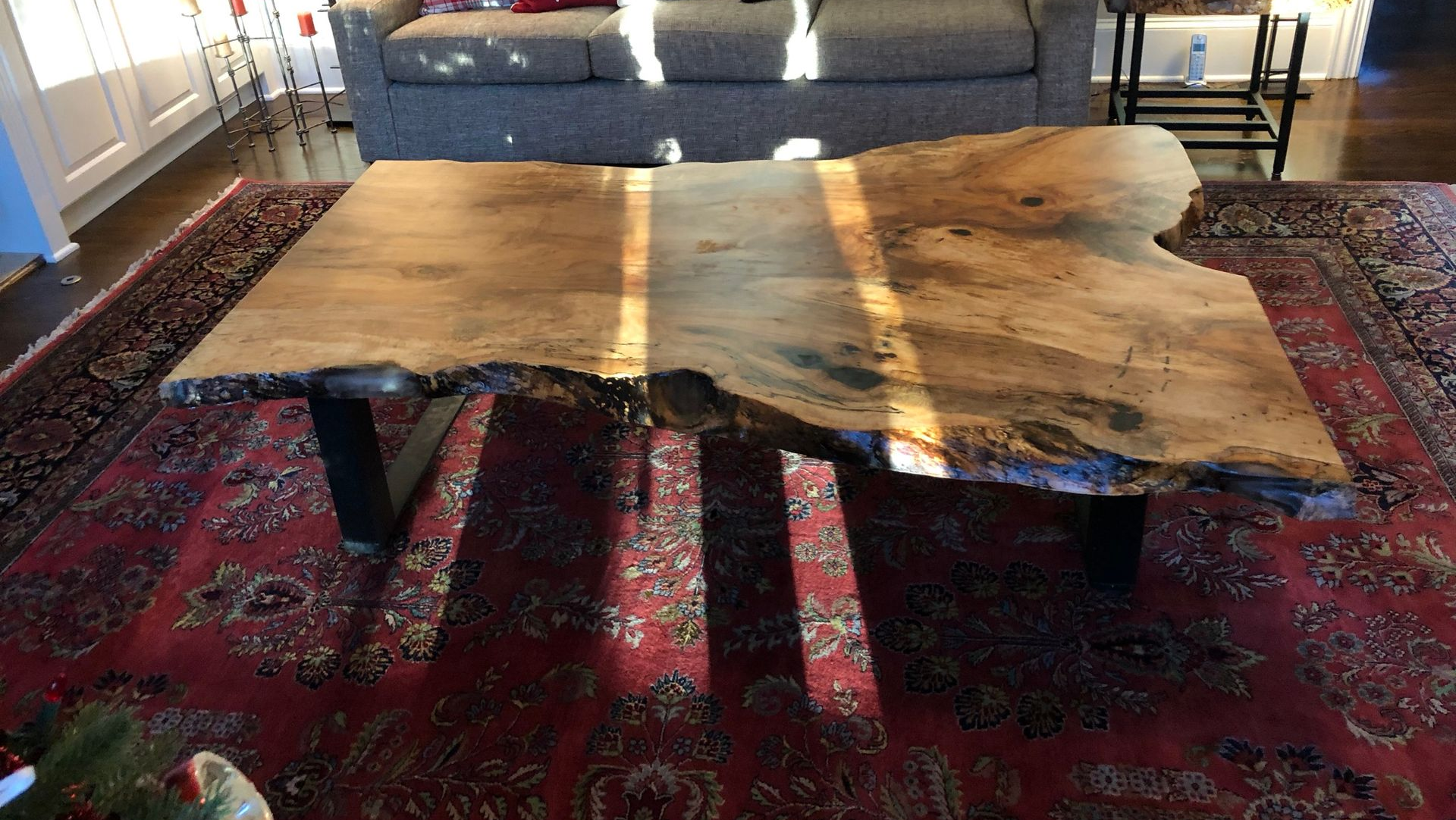 Rustic live-edge wooden coffee table on a red patterned rug in a bright living room