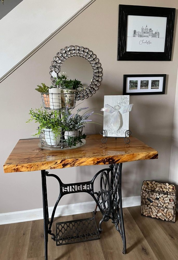 Decorated wooden console table with plants and framed art against a staircase wall