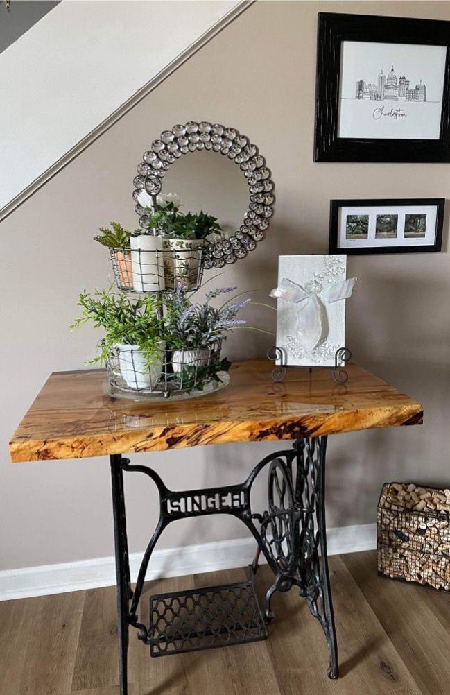 Decorated wooden console table with plants and framed art against a staircase wall