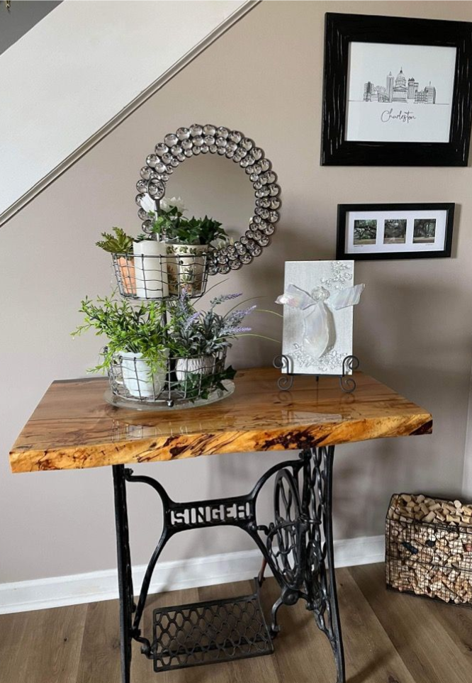 Decorated wooden console table with plants and framed art against a staircase wall