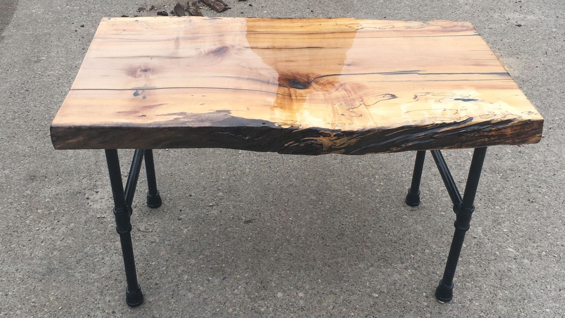 Rough wooden table with black metal legs on pavement, split and weathered at the center.