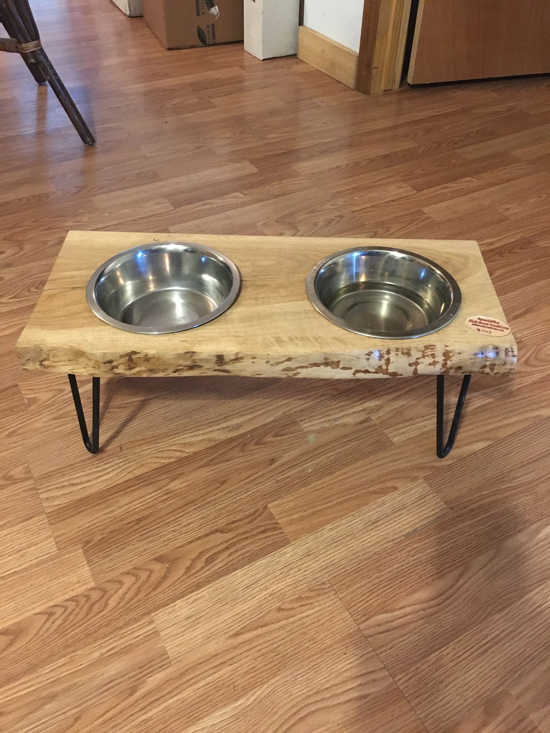 Rustic raised pet feeding station with two metal bowls on a wooden floor.