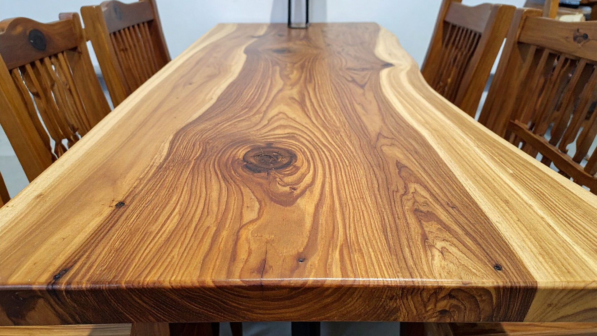 Wooden dining table with a live edge, viewed from one end, surrounded by matching chairs