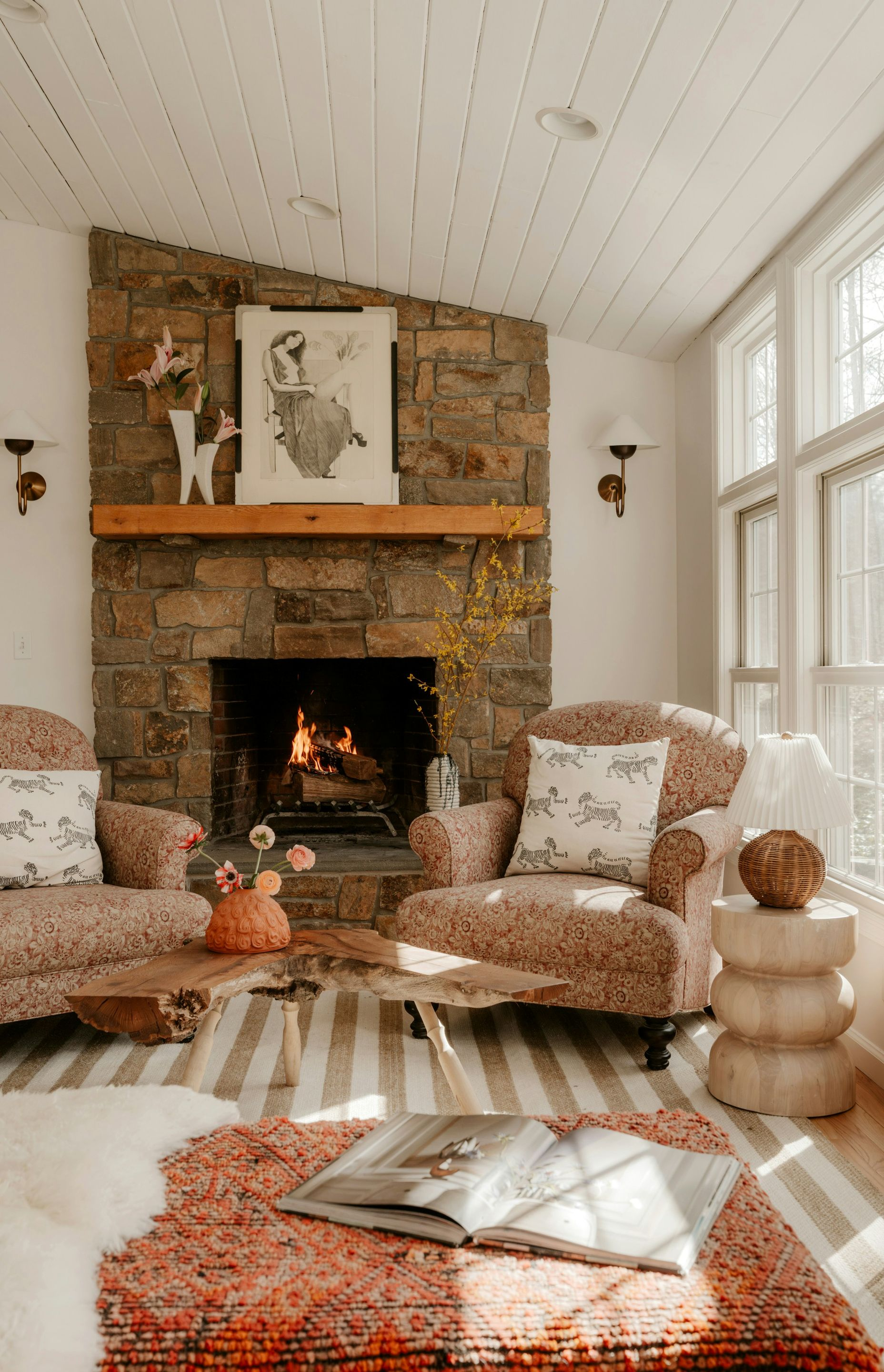 Cozy living room with stone fireplace, upholstered chairs, white walls, and orange patterned rug