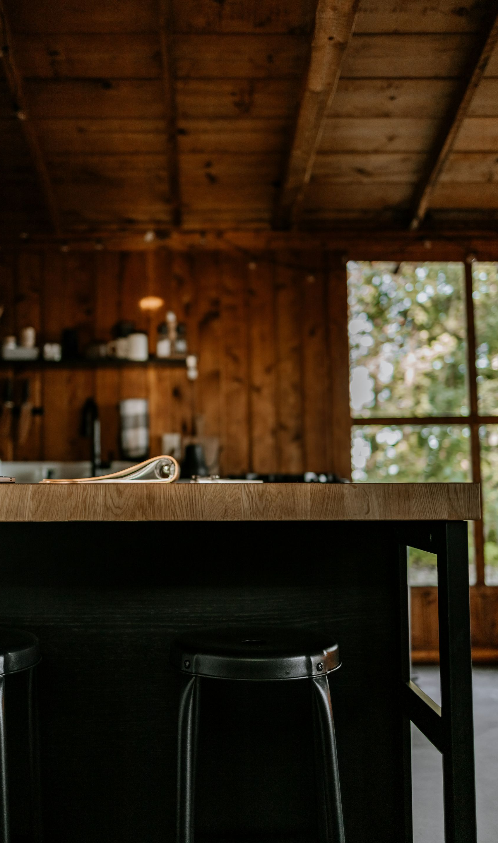 Rustic wooden cabin interior with a table, stool, and sunlight through a window