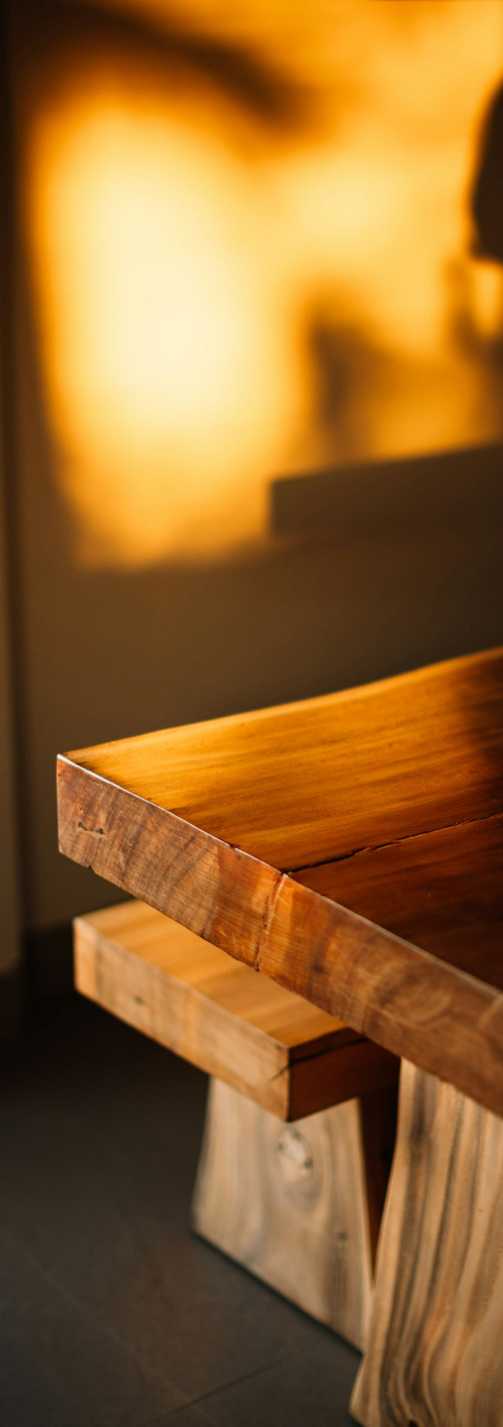 Warm-lit close-up of a wooden table edge with a rustic bench beside it.
