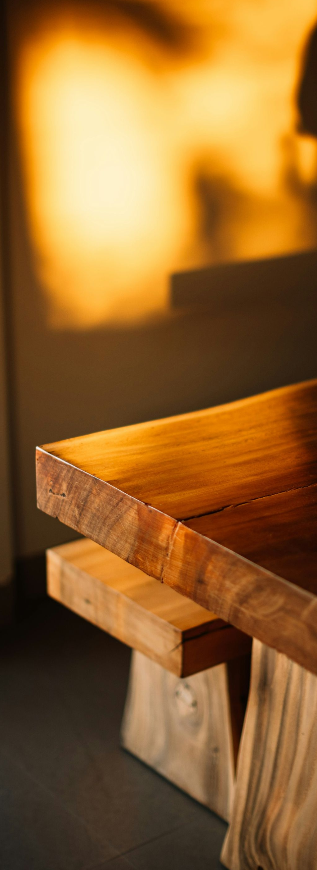 Warm-lit close-up of a wooden table edge with a rustic bench beside it.