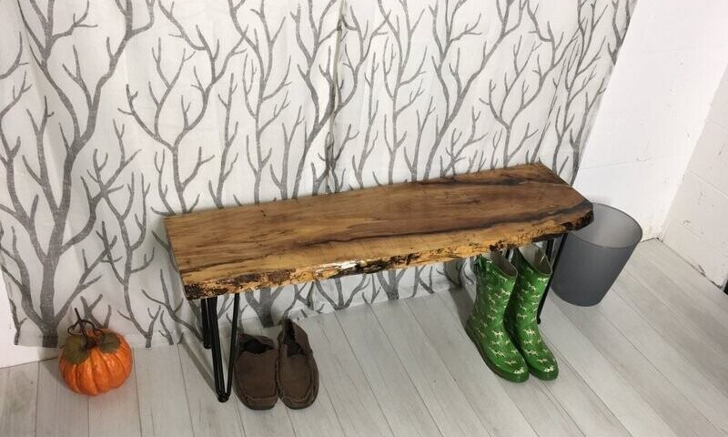 Wooden bench in a corner with boots underneath and a small pumpkin beside it