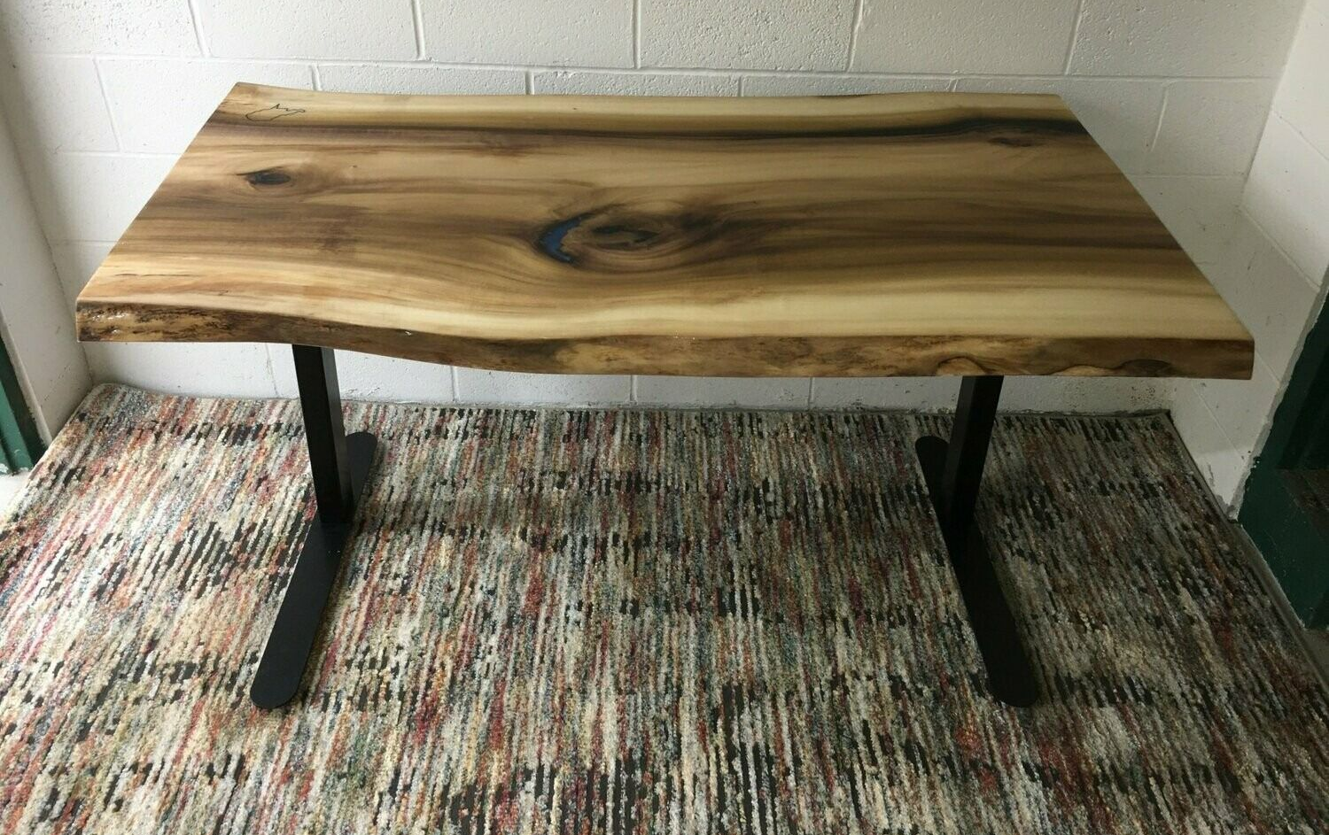 Wood slab table with black metal legs on a patterned rug against a white wall