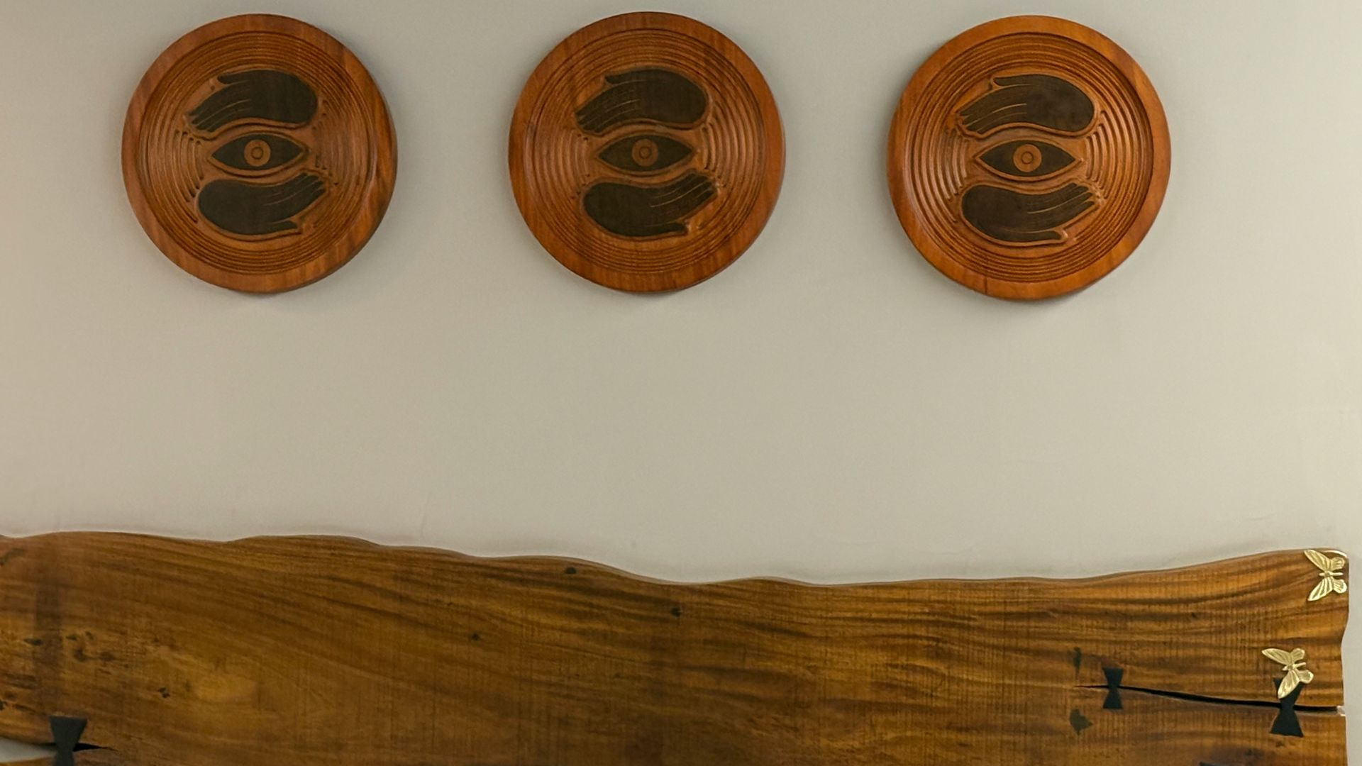 Three carved wooden wall plaques above a long natural wood shelf on a light wall