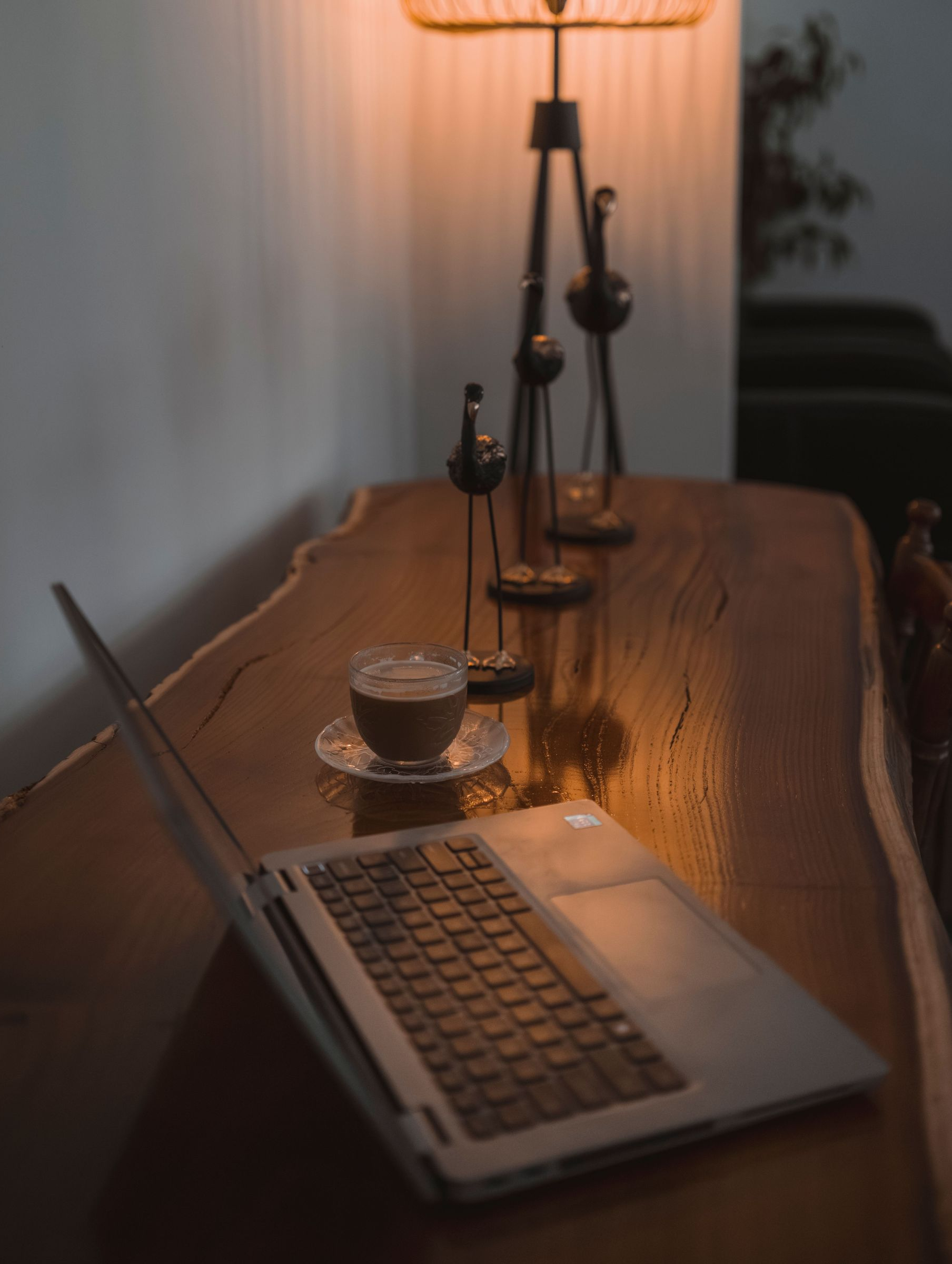 Laptop on a wooden desk beside a coffee cup and candleholders in warm, dim light
