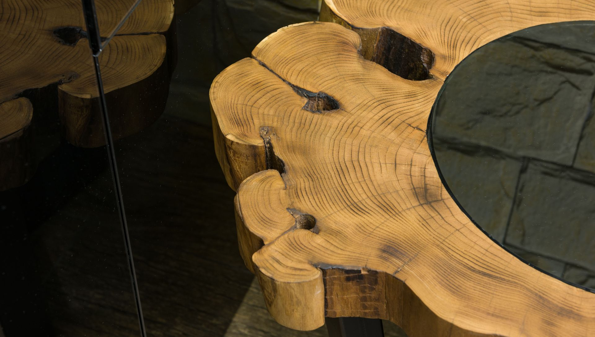 Close-up of round wooden stools with irregular cutout edges and dark leather cushions on a tiled floor