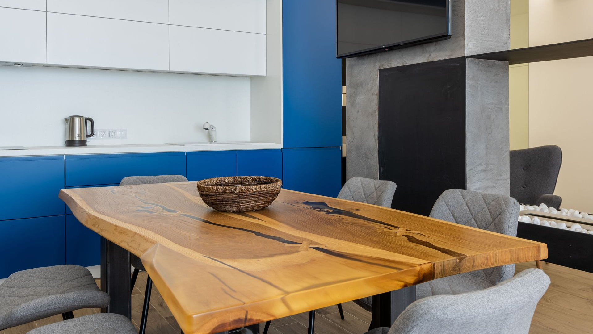Modern dining area with a wooden table, gray chairs, and a bowl centerpiece beside a blue wall.