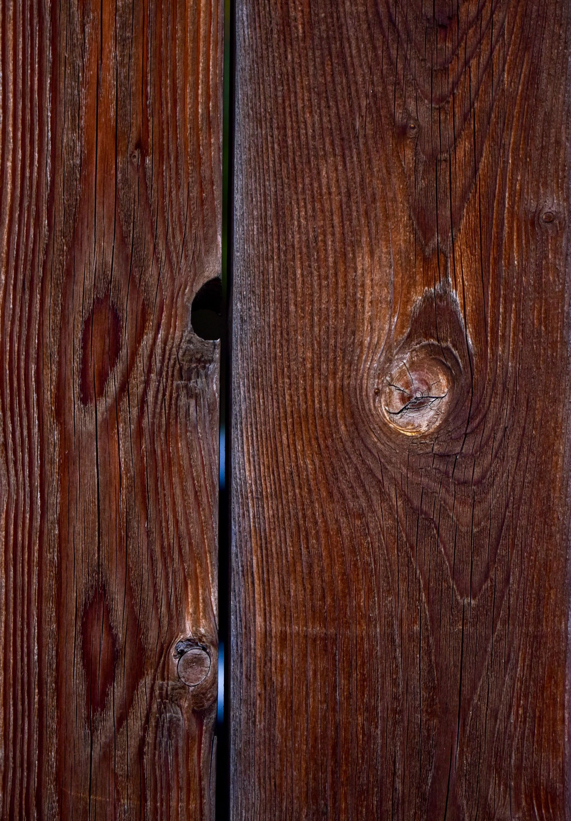 Close-up of weathered brown wooden boards with knots and a narrow vertical gap between them