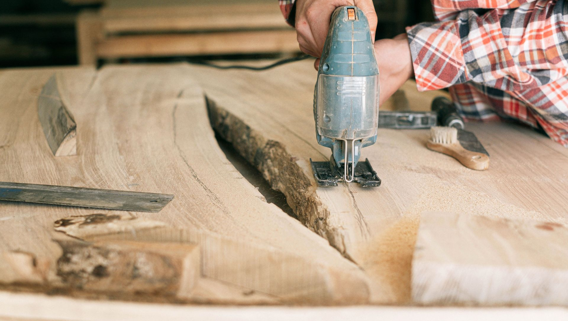 Person using a jigsaw to cut a wooden board in a workshop