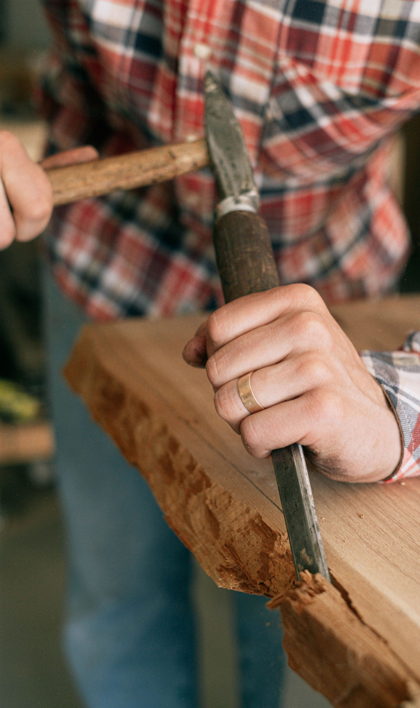 Person chiseling wood with a hammer and chisel on a timber beam in a workshop