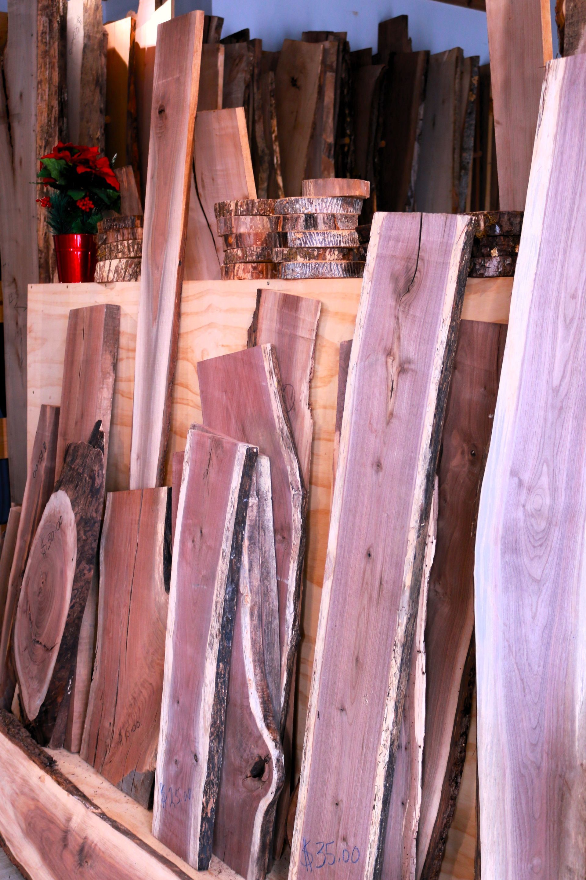 Stacked wooden planks in varied colors and textures, leaning upright in a workshop or lumber yard.