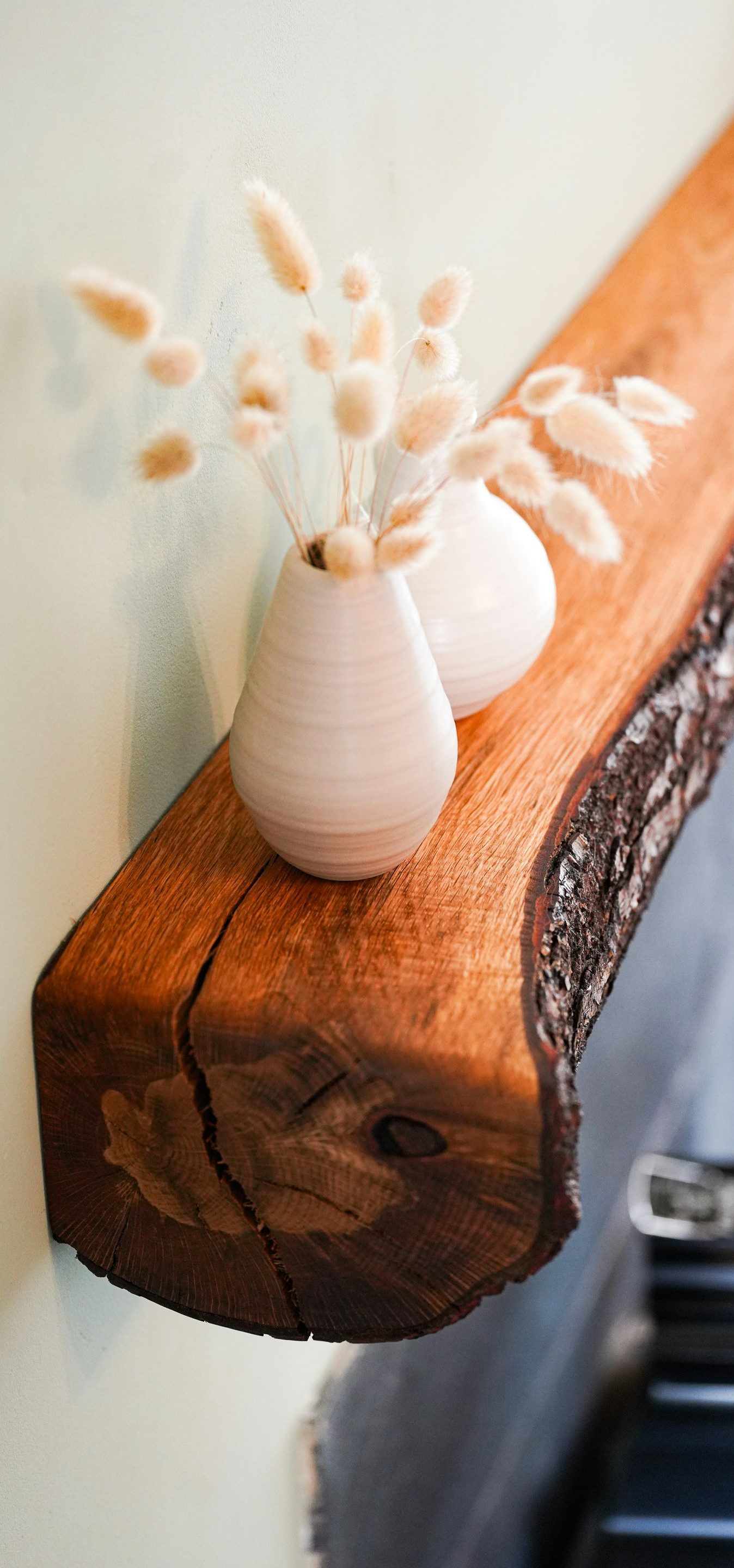 Small white vase with dried flowers on a rustic wooden shelf