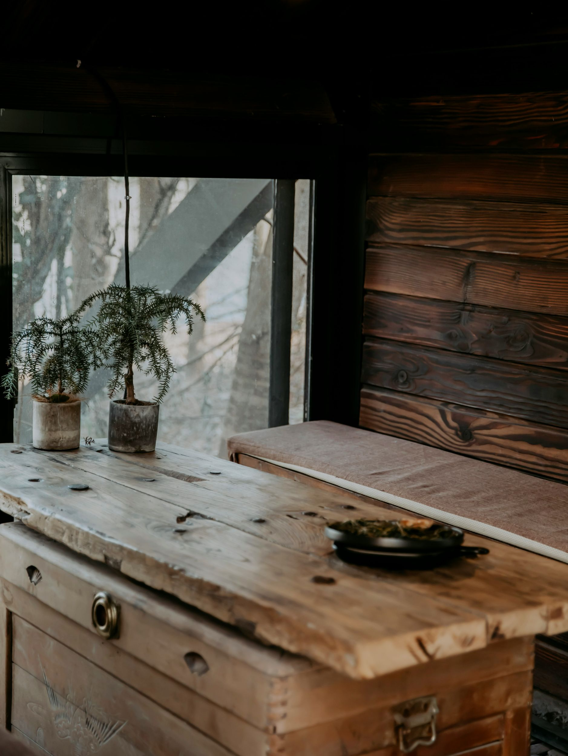 Rustic wooden desk by a window with potted plants and a notebook on top