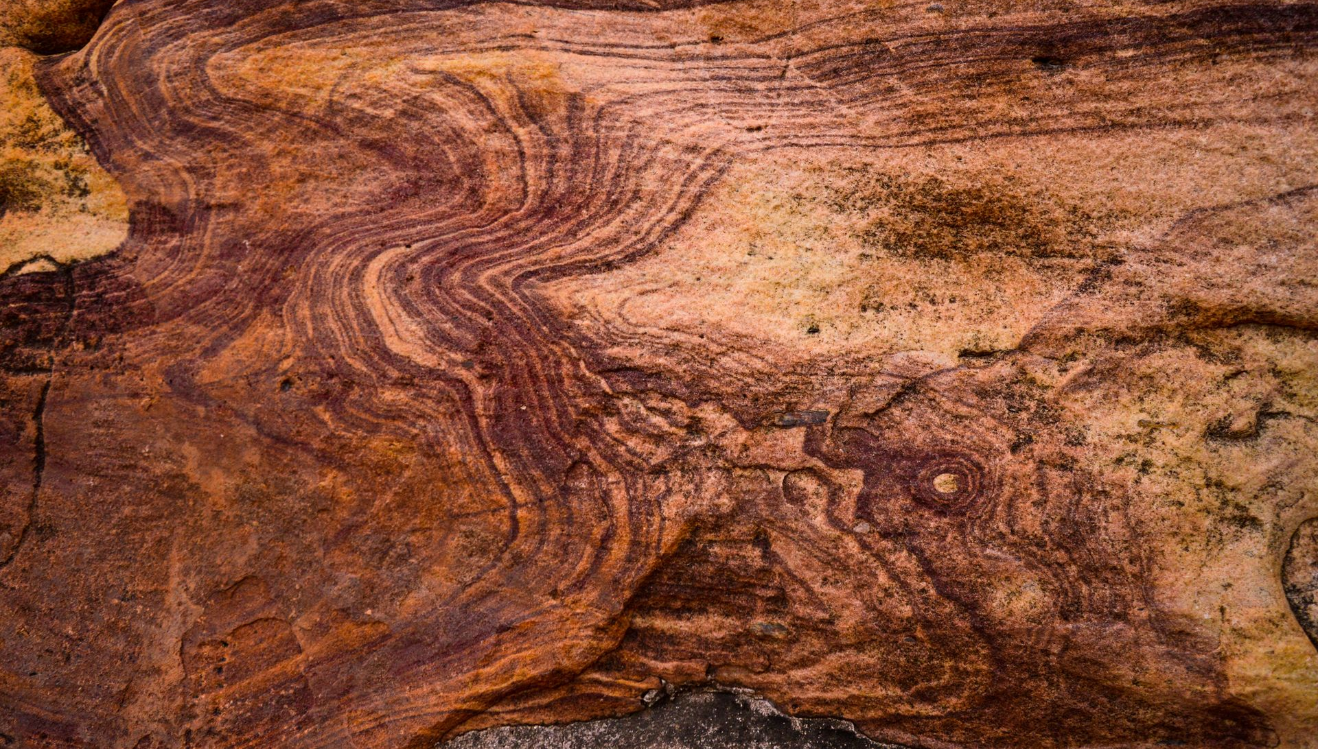 Striated reddish-brown rock surface with swirling sediment layers and weathered texture