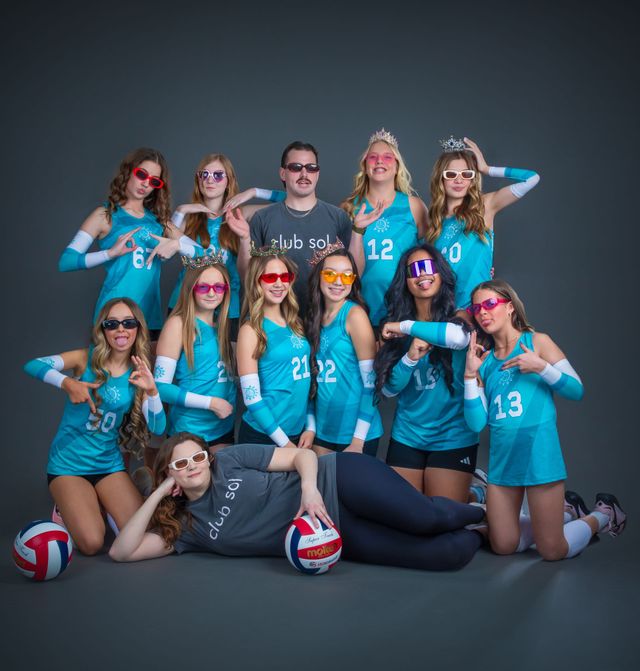Volleyball team posing in teal jerseys with two volleyballs on a studio gray background