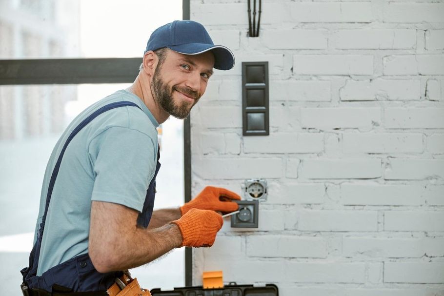 Smiling worker in blue shirt and orange gloves installing a fixture on a white wall