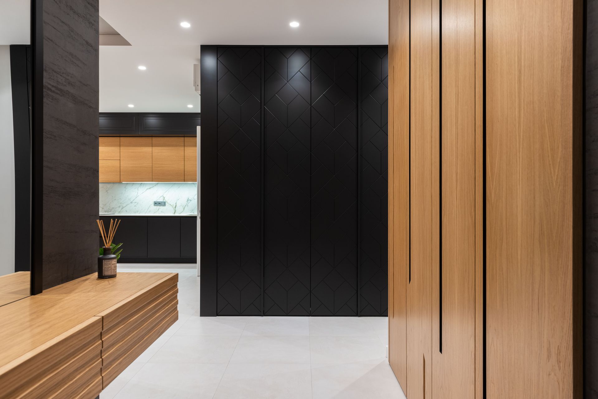 Modern entryway with black and wood-paneled walls, built-in bench, and polished white floor