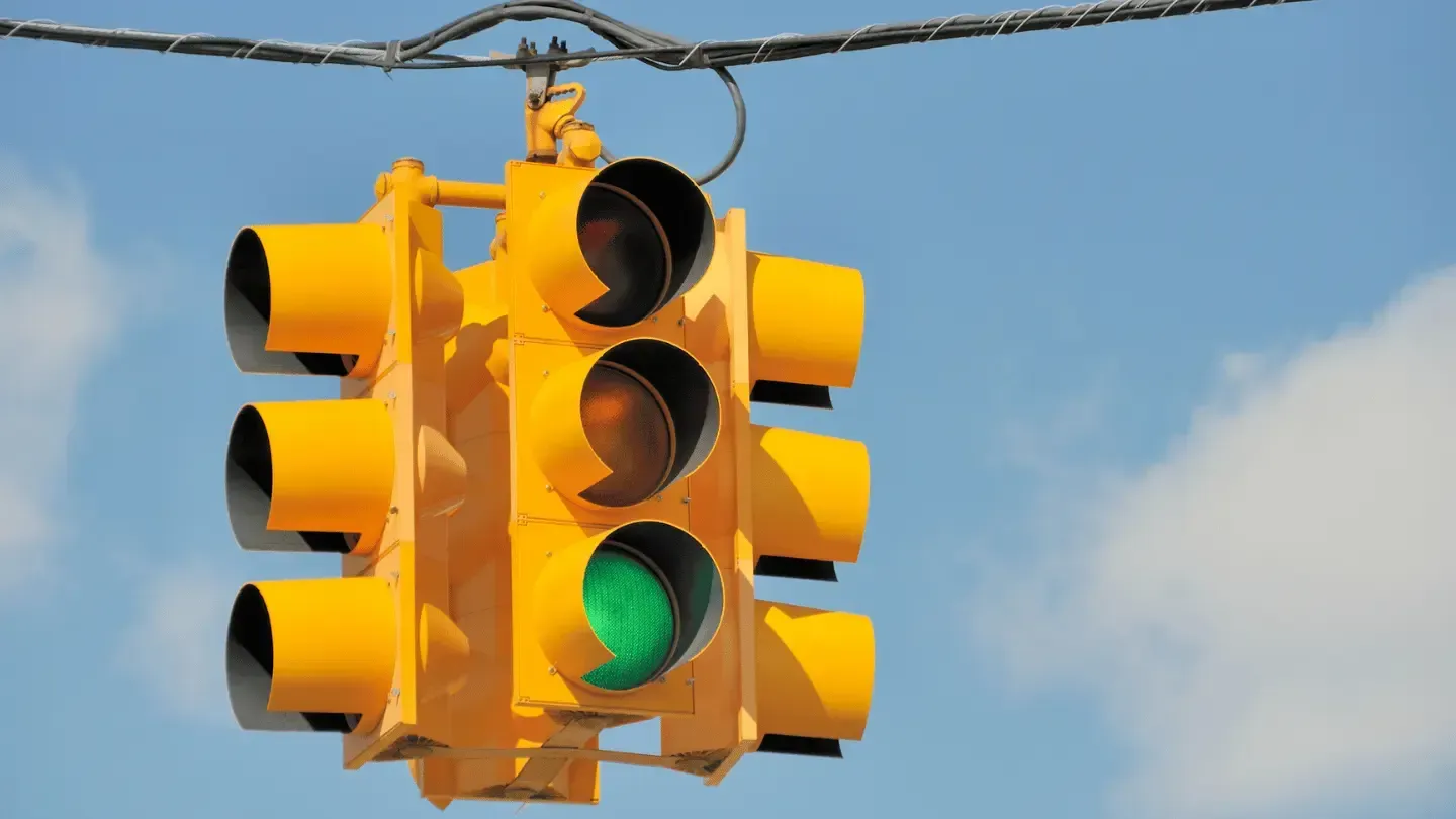 A yellow traffic light with a green light hanging from a wire