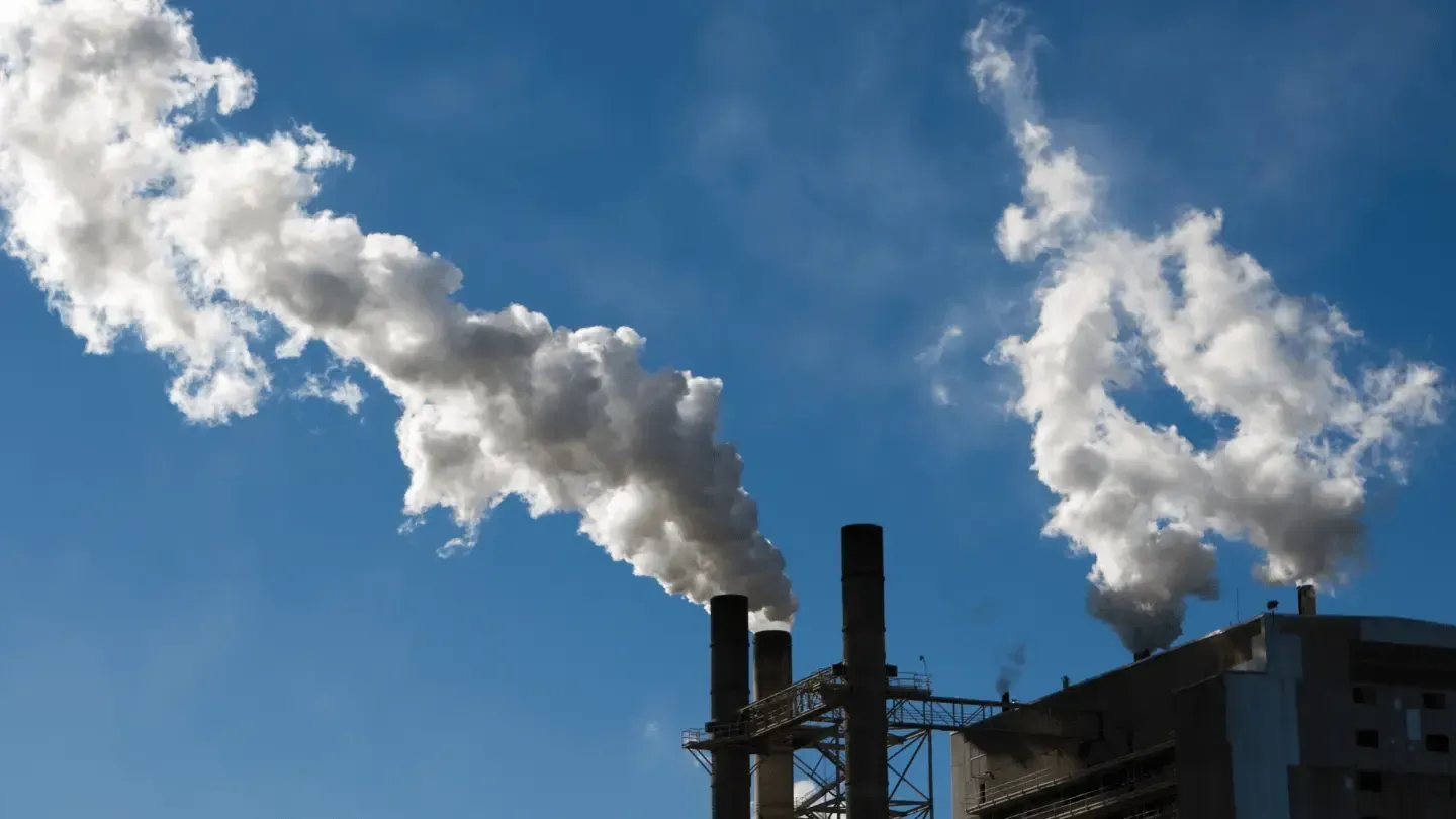 Smoke is coming out of two chimneys of a factory against a blue sky.