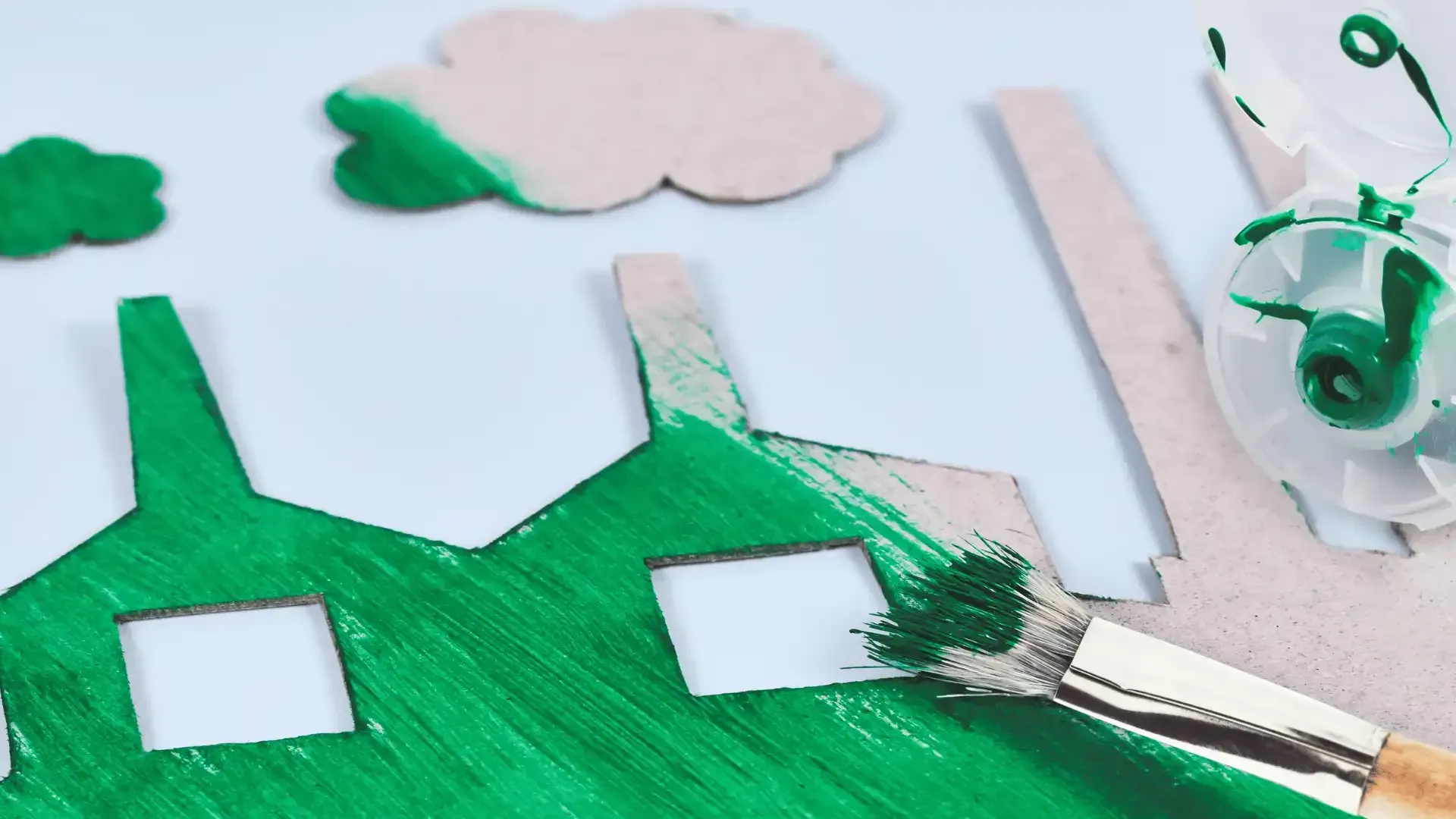 A green house is being painted with a brush.