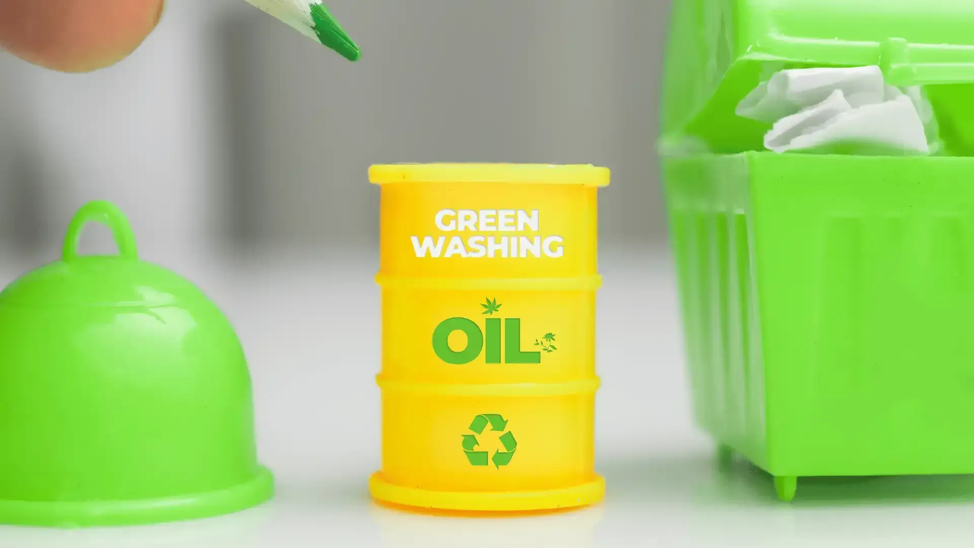 A person is holding a green pencil next to a yellow barrel that says `` green washing oil ''.