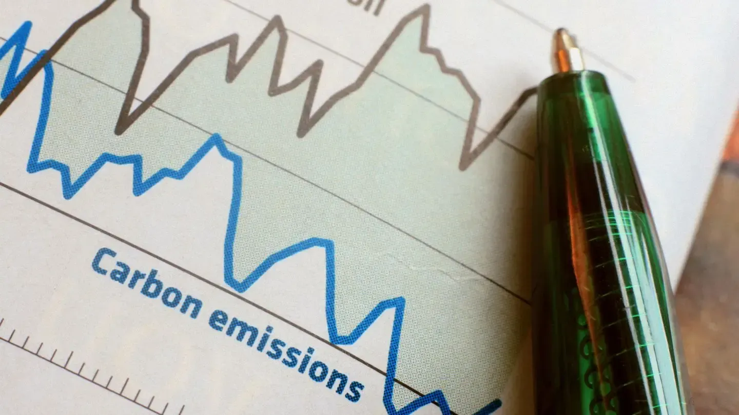 Graph showing carbon emissions, with blue and gray lines fluctuating, a pen pointing at the graph.