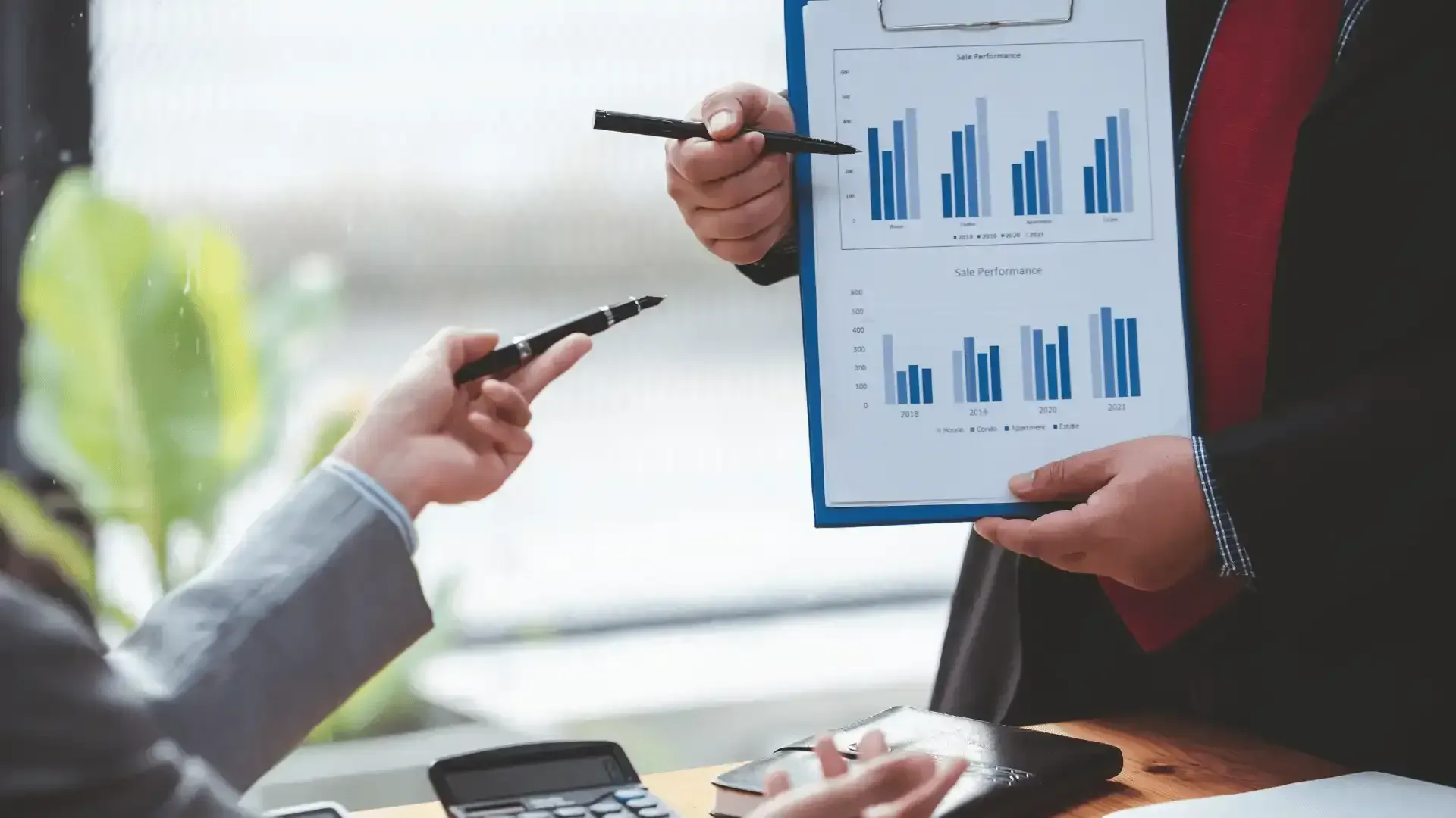 A man is pointing at a graph on a clipboard while a woman looks on.