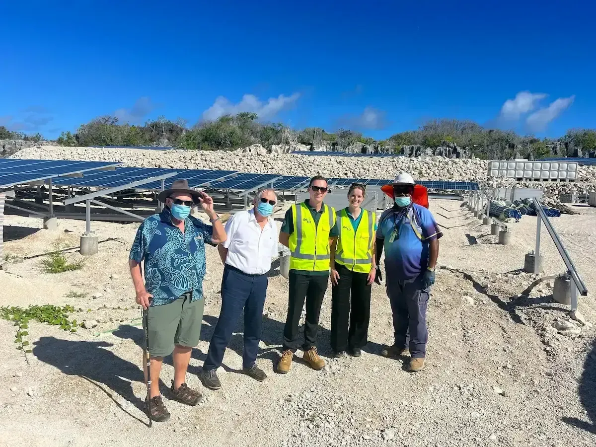 A group of people are posing for a picture in front of a solar panel.