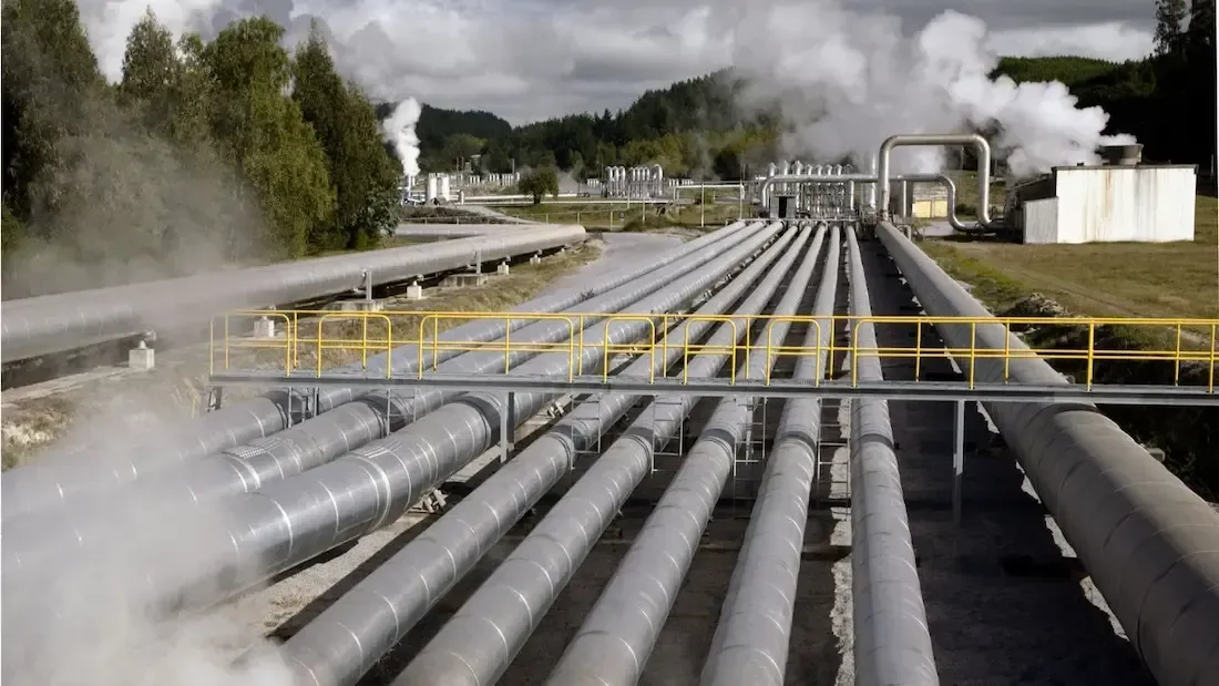 Geothermal power plant with steam rising from insulated pipes, set in a natural landscape.