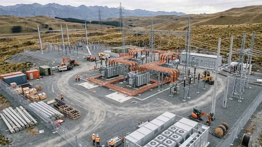 Electrical substation under construction with steel towers, transformers, and orange equipment on a gravel site