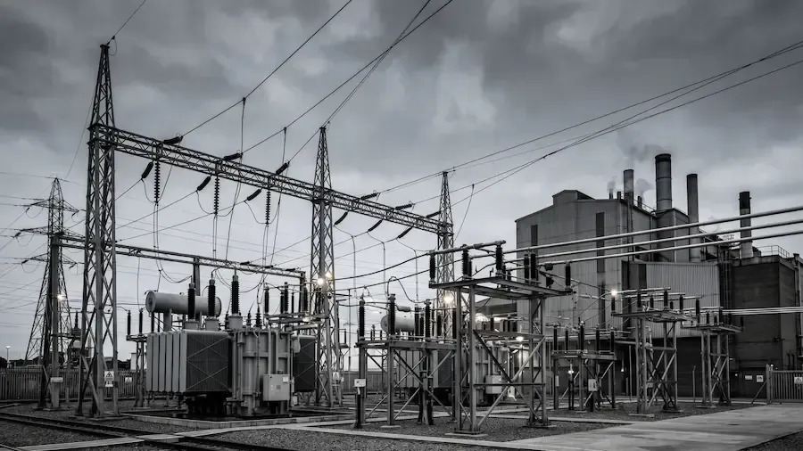 Industrial power substation with transformers, metal structures, and overhead power lines under a gray sky