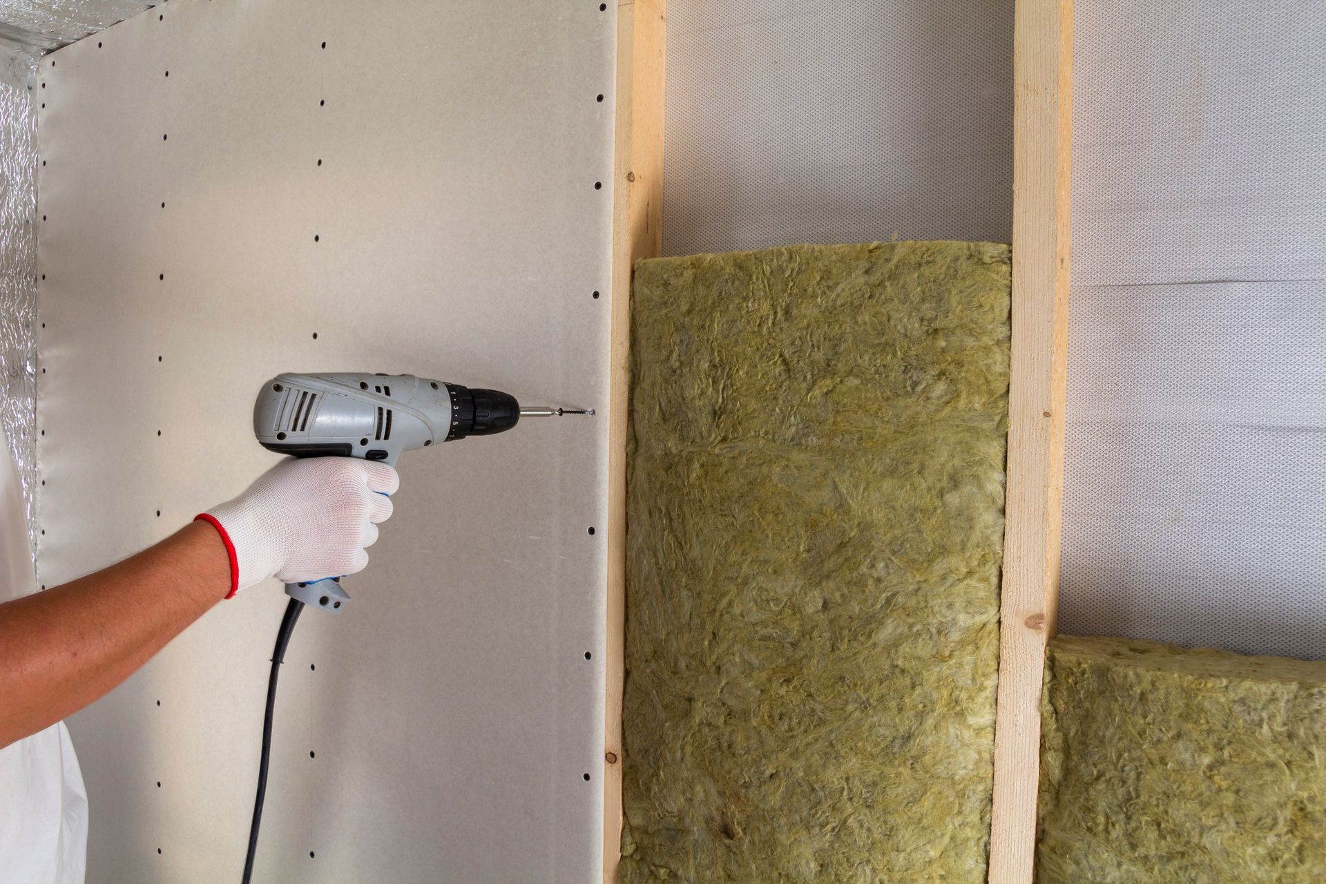 A person is using a drill to install insulation on a wall.