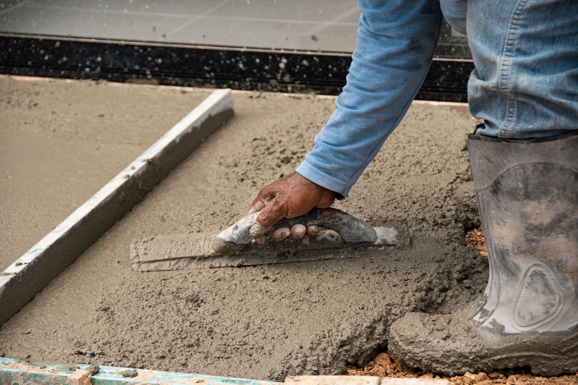 A man is spreading concrete on the ground with a trowel.