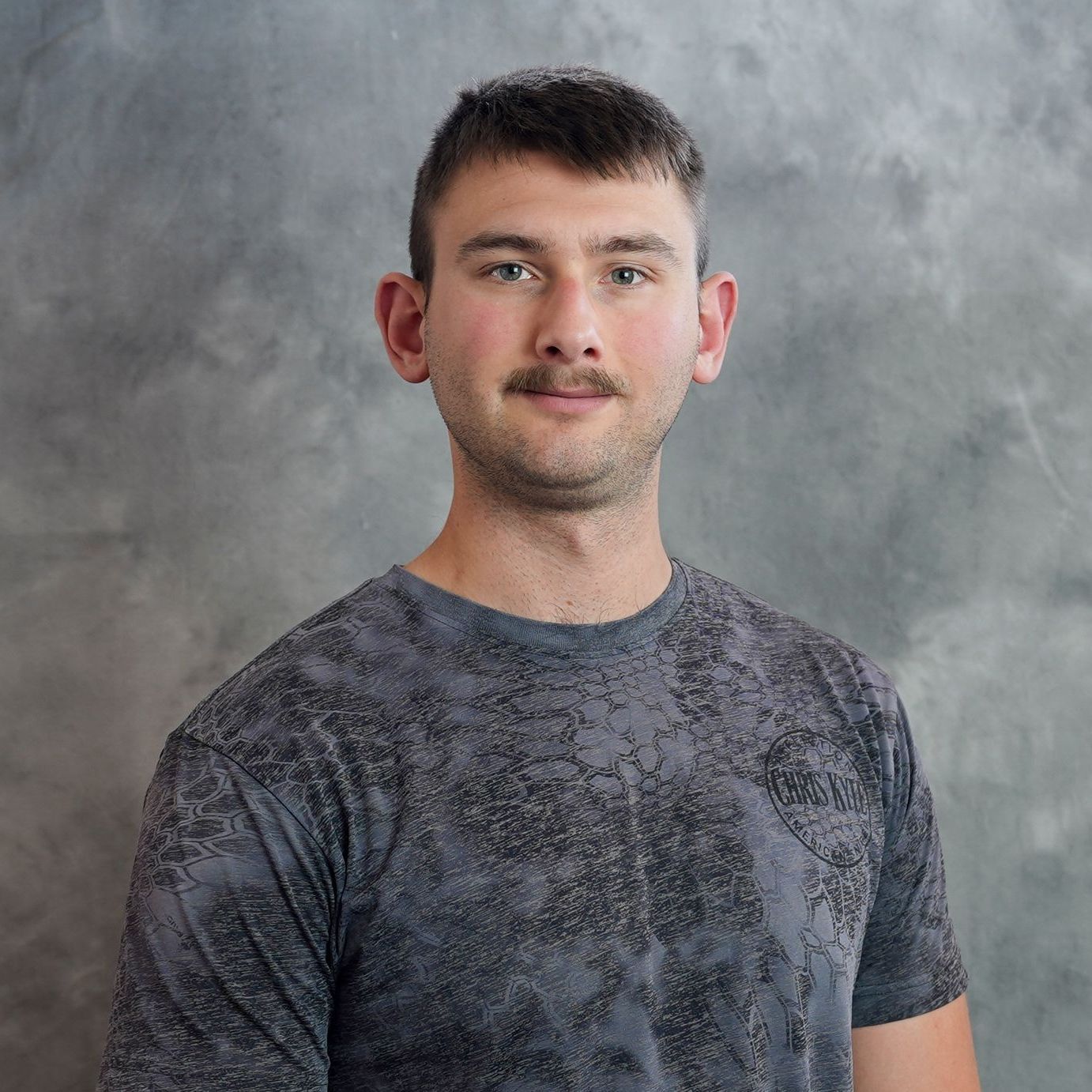 A young man with a mustache is wearing a gray t-shirt.
