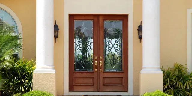 Wooden double front doors with decorative glass in a beige stucco entryway