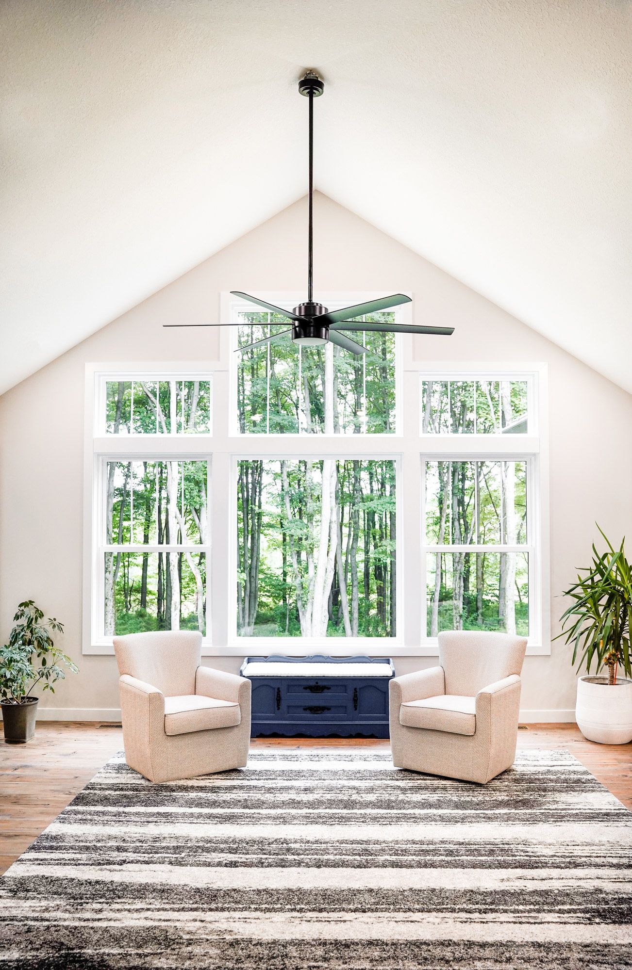 Bright airy living room with vaulted ceiling, tall windows, two chairs, a blue bench, plants, and a striped rug
