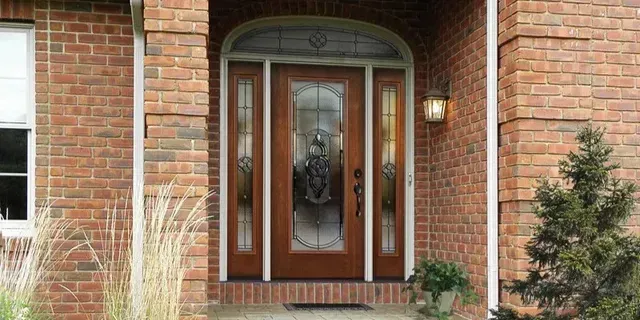 Brick house front door with glass panels, brick walkway, and porch lights surrounded by landscaping