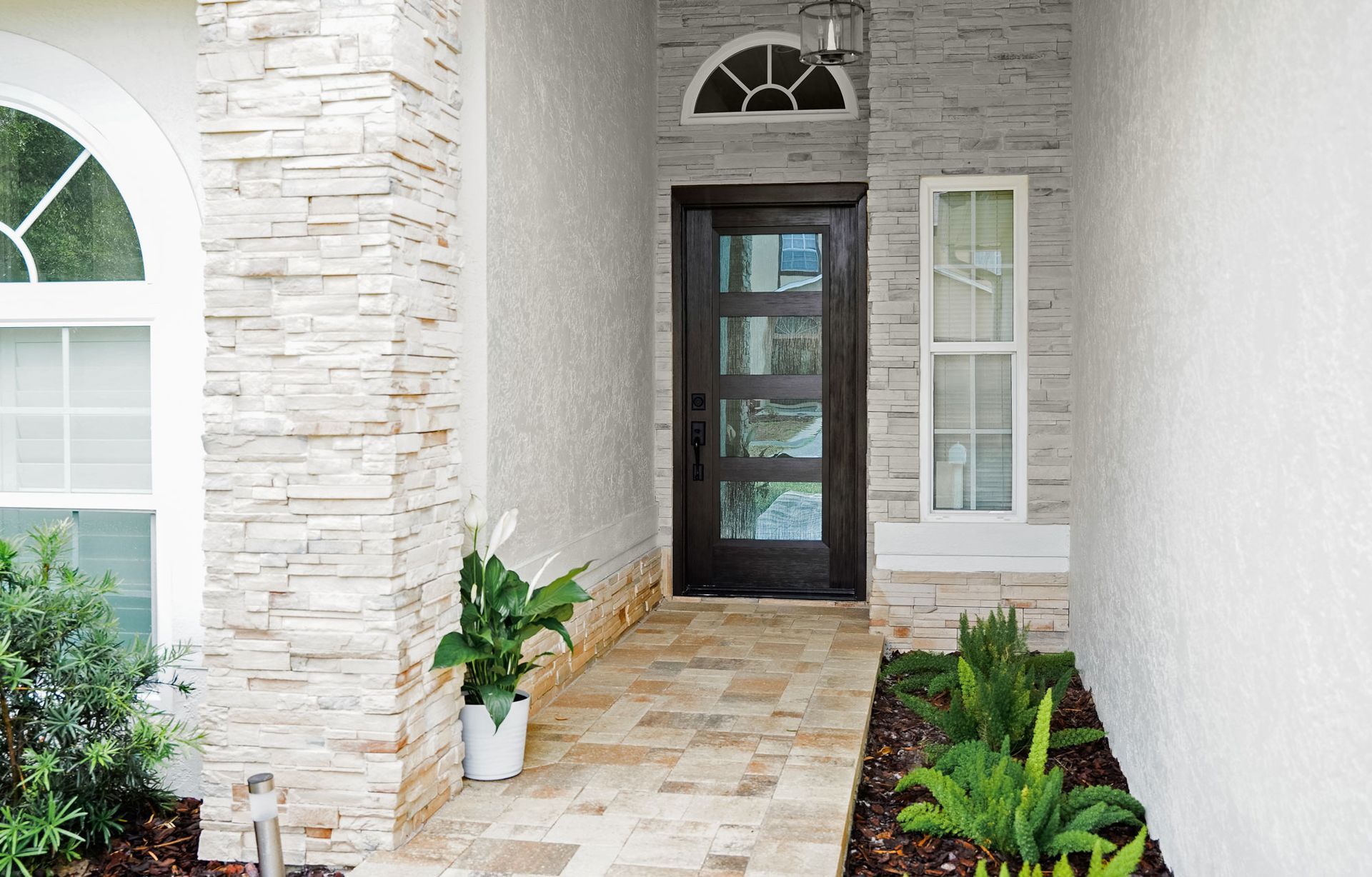 Front porch with stone columns, glass front door, and potted greenery in a bright entryway