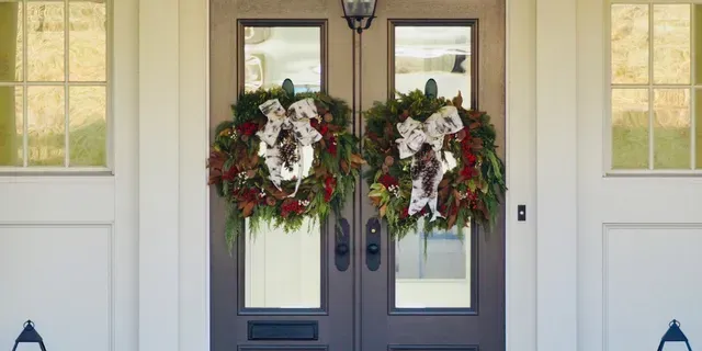 Front door with two Christmas wreaths and white sidelights on a home exterior