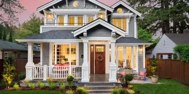 Two-story gray house with a lit front porch, white trim, and a front yard at dusk