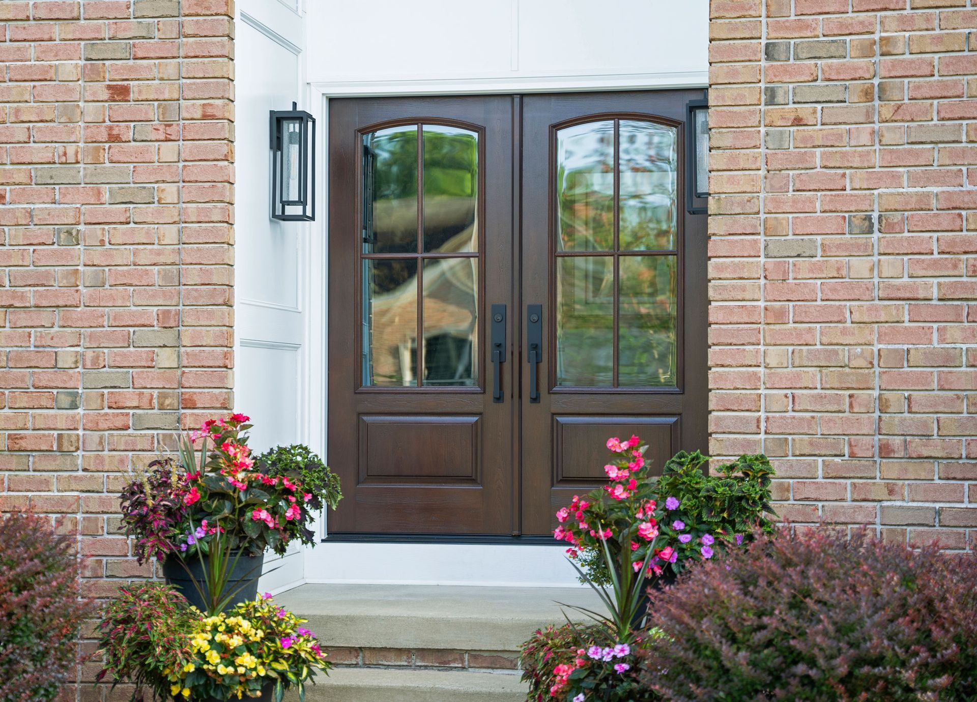 Front entrance with dark wood double doors, brick walls, and flower beds on both sides.