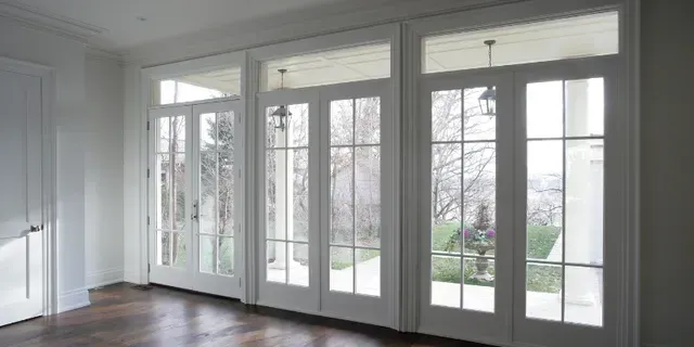 Bright empty room with white walls and large French doors opening to a garden.