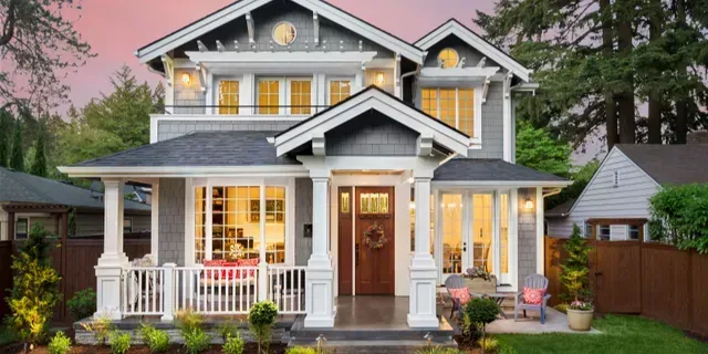 Two-story gray house with white trim and a lit front porch at dusk