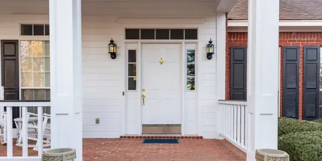 Front porch with white double doors, brick steps, black lanterns, and railings on either side.